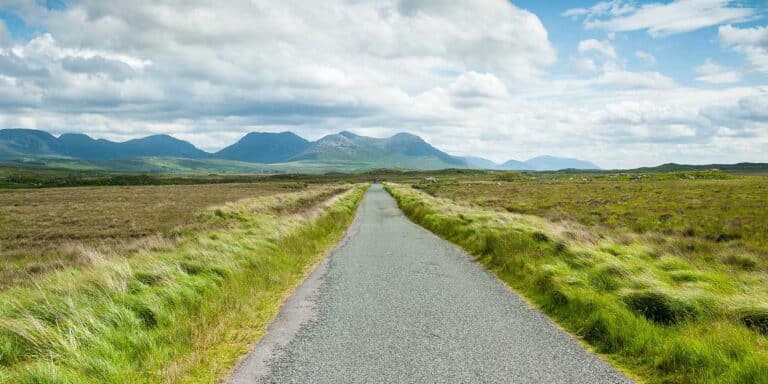 A narrow country road winds through grassy fields, perfect for a Clifden Bike Hire adventure.