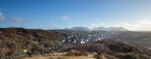 A panoramic view of a quaint town nestled amidst lush hills under a vast, clear sky.