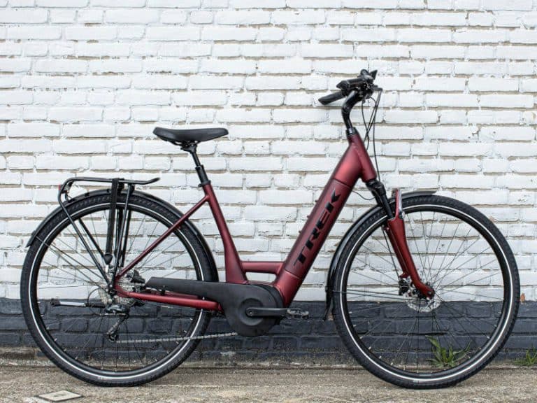 Red step-through electric bike parked against a white brick wall.