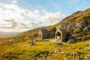 Ancient stone chapel nestled in a tranquil hillside, basking in the golden light of the sun, as a testament to times long past amidst the serene beauty of rolling landscape.
