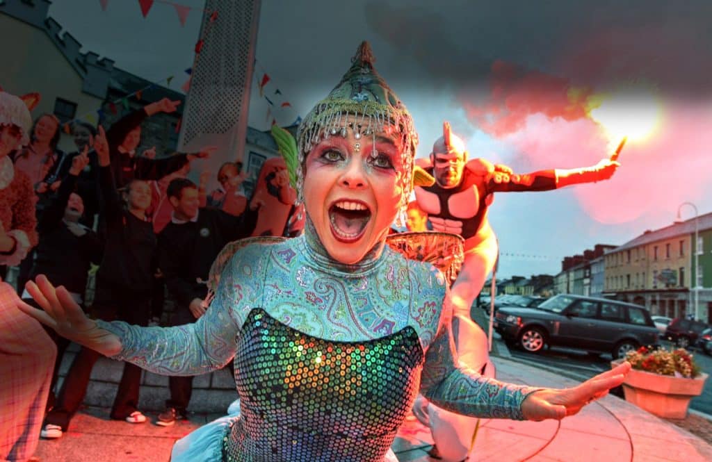 A performer in a colourful costume smiles widely at a lively Celebration of Arts and Culture.