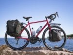 Trek 520 Disc touring bike with pannier bags parked on rocks by water under a blue sky.