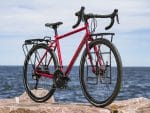 Trek 520 Disc touring bike with black racks, parked on rocks by the sea under cloudy skies.