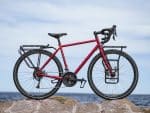 Red Trek 520 Disc touring bike with racks parked on rocks by the sea under a cloudy sky.