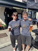 Two women outside Clifden Bike Hire bar, smiling in matching Life is Good in Connemara T-shirts.