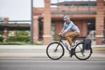 Cyclist with a Bontrager Commuter Single Pannier 16.5 L rides past a brick building in the city.