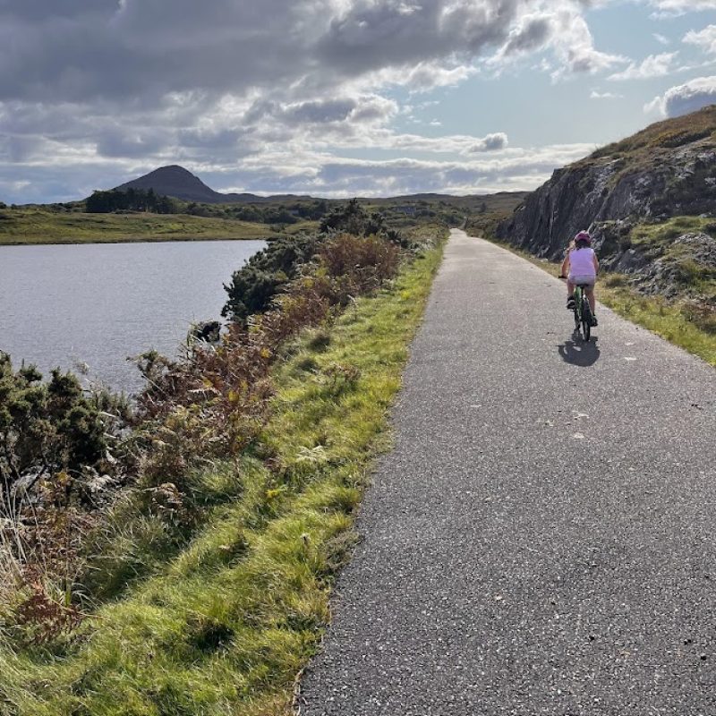 A serene bike ride beside a tranquil lake under a vast, cloud-streaked sky, with rolling hills in the distance.