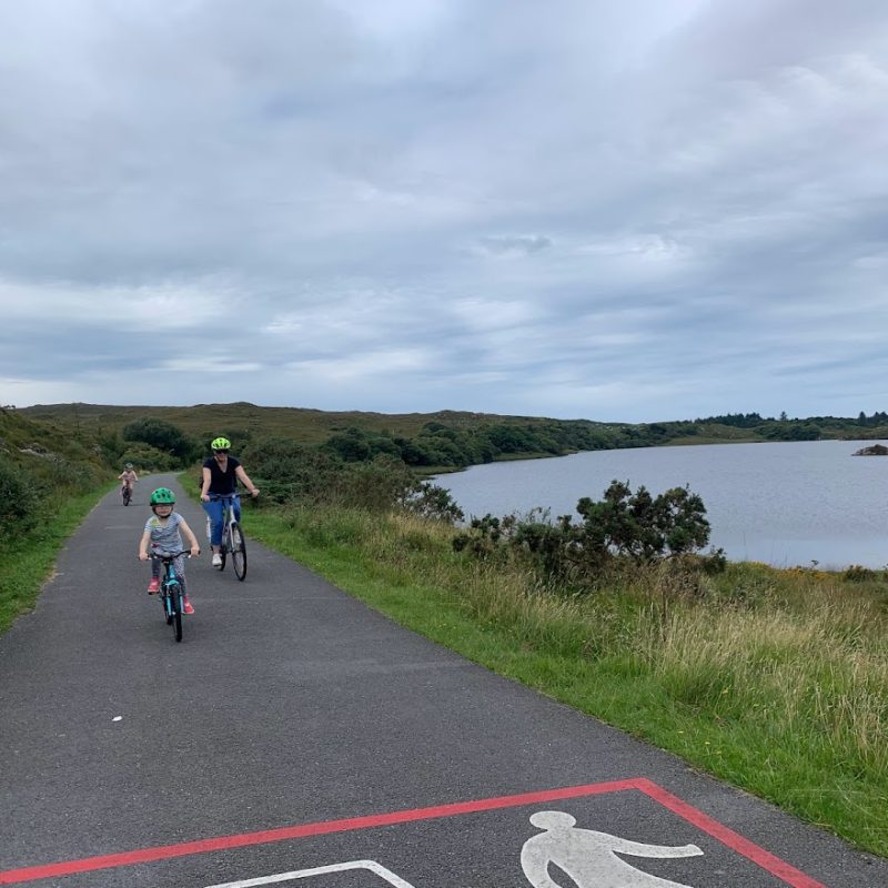 A family enjoys a pleasant bike ride along a serene lakeside path under cloudy skies.