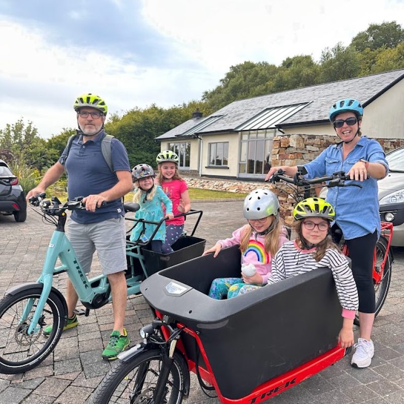 A family ready for a cycling adventure, with the parents on cargo bikes equipped with child seats, and kids wearing helmets for safety.